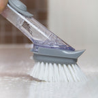 Gray dishwashing brush with bristles and a clear handle cleaning a surface.