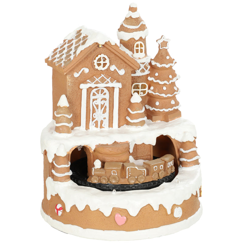 Musical gingerbread house Christmas decoration with snowy roof, trees and miniature train on a white background