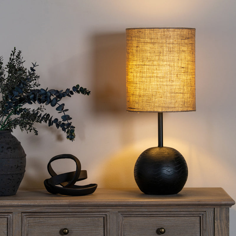 Black ball table lamp lit on a sideboard with dark vases