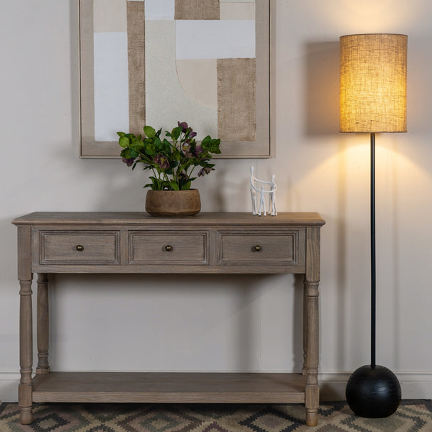 Black floor lamp lit beside a wooden console table