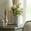 Bloomville vase with pink roses on a side table by a window