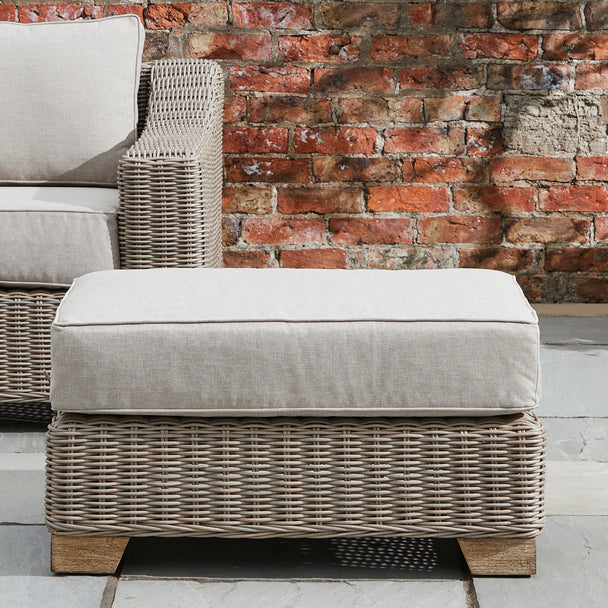 Capri footstool on a patio beside a wicker armchair