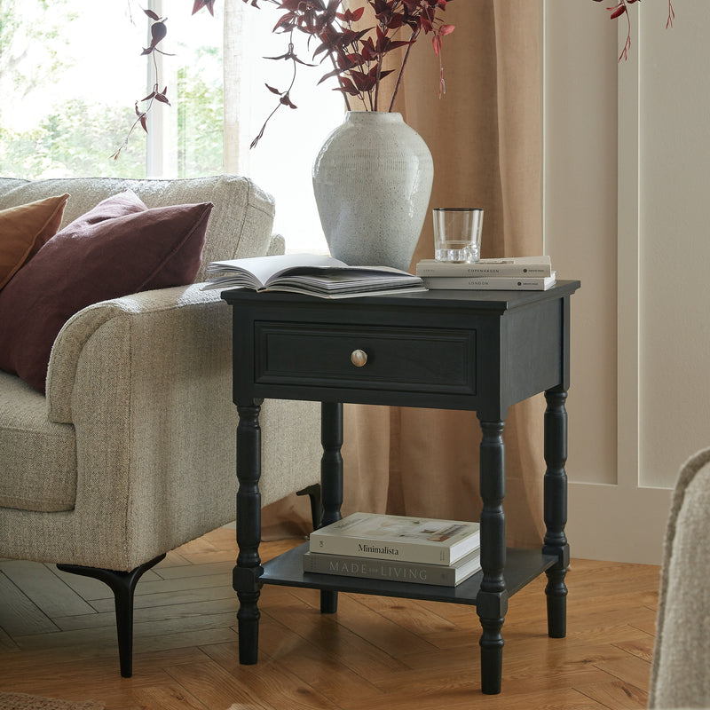 Contour black side table beside a sofa with a vase on top