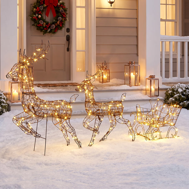 3-Piece Rattan Reindeer and Sleigh Christmas Light Set illuminated outside a decorated home