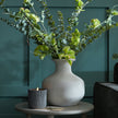 Darcy squat vase with faux greenery against a dark green wall