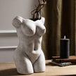 Female figure vase with dried branches on a wooden shelf