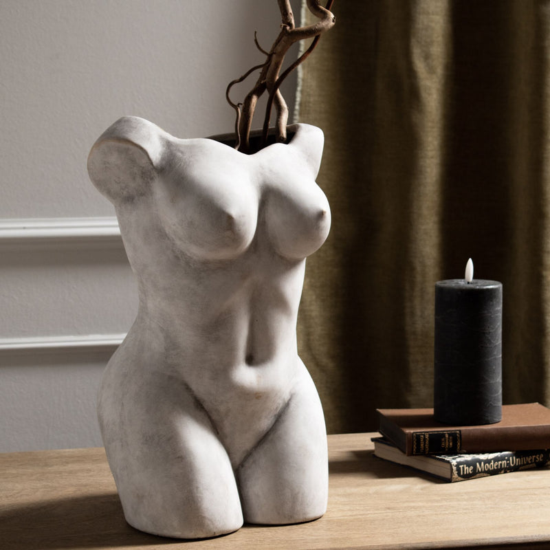 Female figure vase with dried branches on a wooden shelf