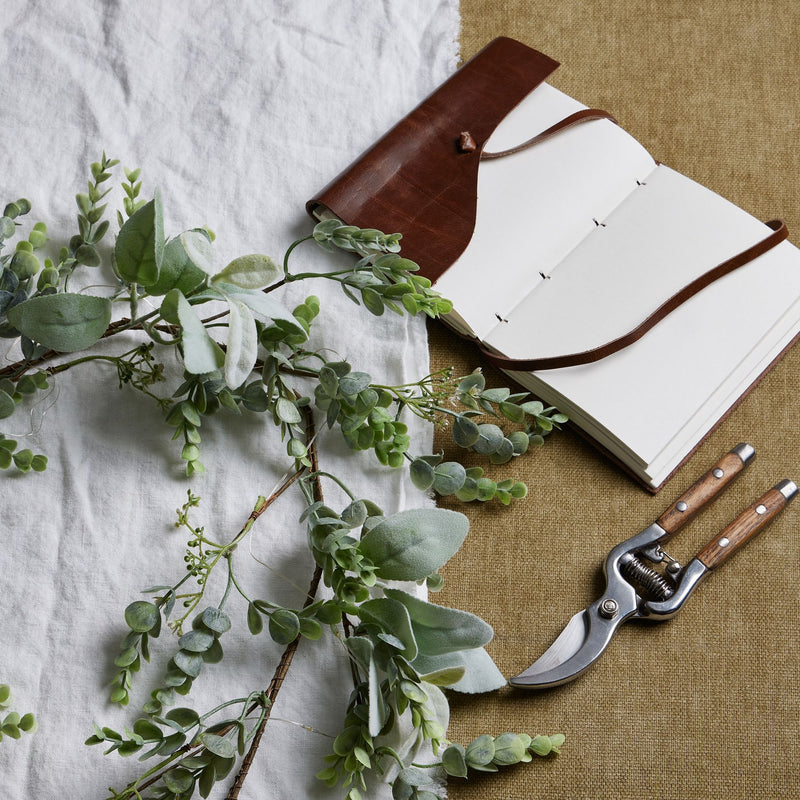 Winter garland laid on a table beside a notebook and secateurs
