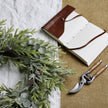 Frosted wreath beside a leather notebook and secateurs