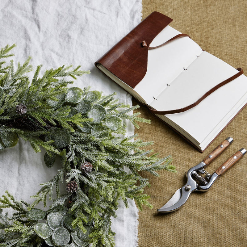 Frosted wreath beside a leather notebook and secateurs
