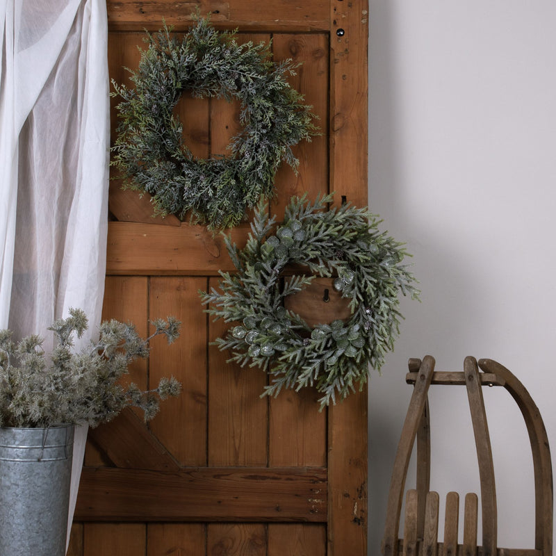 Frosted Pine Christmas Wreath with Pinecones – 55cm, two frosted wreaths hung on a wooden door