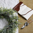 Frosted Pine Christmas Wreath with Pinecones – 55cm, wreath laid on a table beside a notebook and secateurs