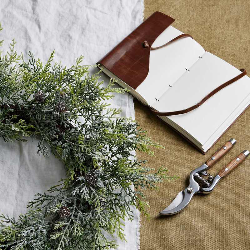 Frosted Pine Christmas Wreath with Pinecones – 55cm, wreath laid on a table beside a notebook and secateurs