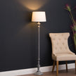 Ithaca floor lamp lit beside an upholstered chair against a dark wall