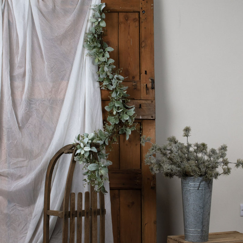 Winter garland draped over a rustic wooden door beside a chair