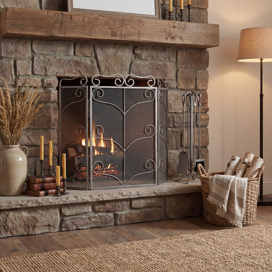 Antique silver ornate fire screen in front of a lit stone fireplace