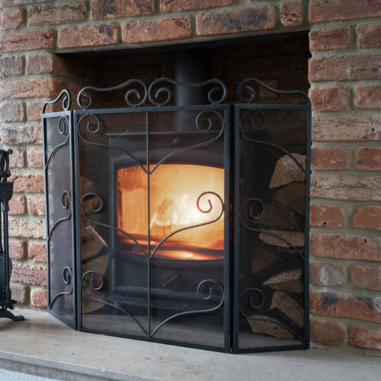 Black ornate fire screen in front of a wood burner in a brick fireplace