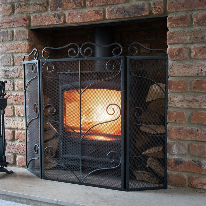 Black ornate fire screen in front of a wood burner in a brick fireplace