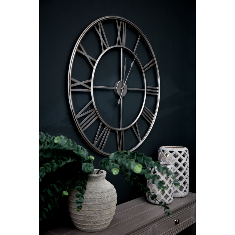 Silver skeleton clock on a dark wall above a sideboard