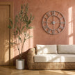 Silver skeleton clock on a pink wall above a wicker sofa