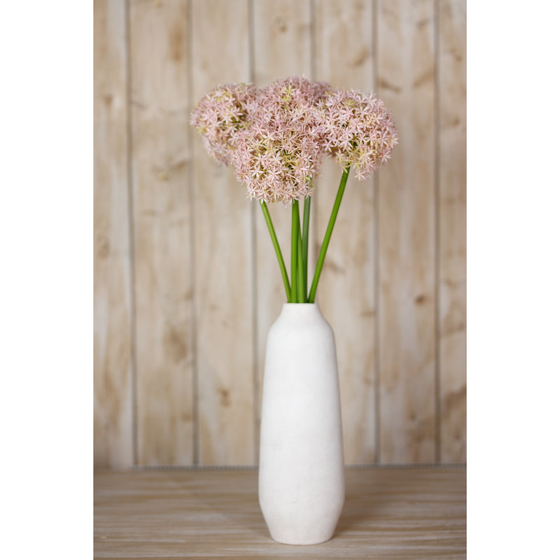 lilac alliums in a tall white vase against a wooden wall