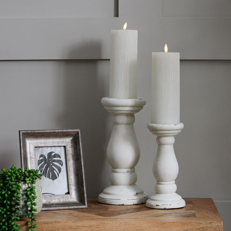Two white column candle holders with LED candles beside a framed print