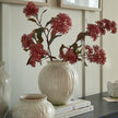 Numa round vase with red stems on a sideboard