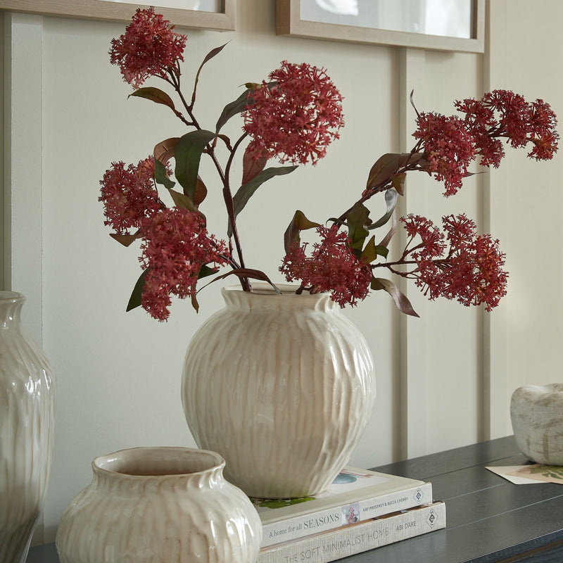 Numa round vase with red stems on a sideboard