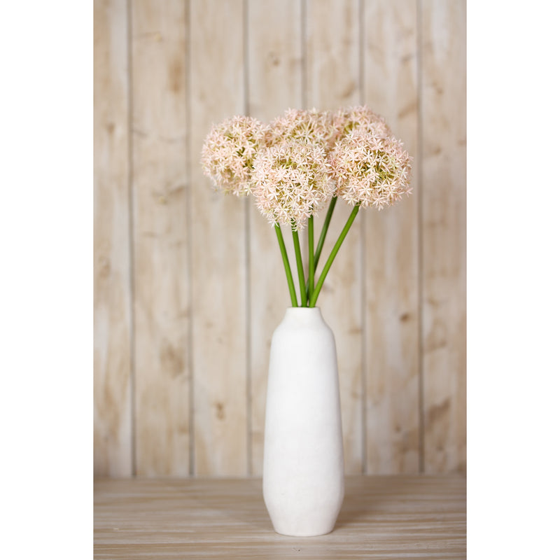 pink alliums in a tall white vase against a wooden wall