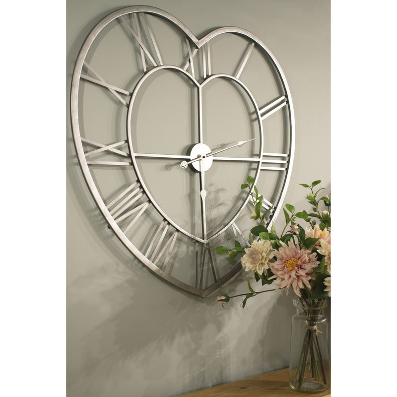 Silver heart wall clock hanging on a wall beside flowers