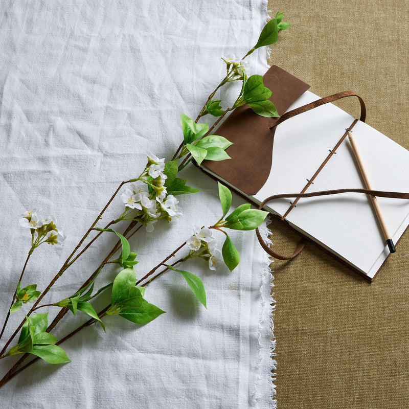mock orange stems laid on linen with a leather bag