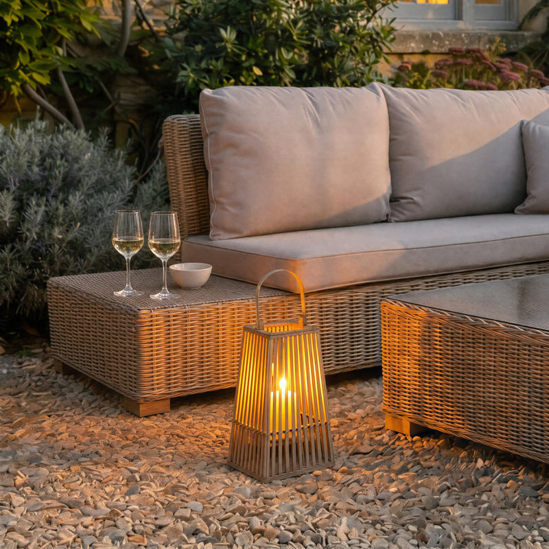 Tapered wicker lantern glowing beside a rattan sofa set