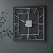 Grey square clock on a dark wall beside trailing greenery