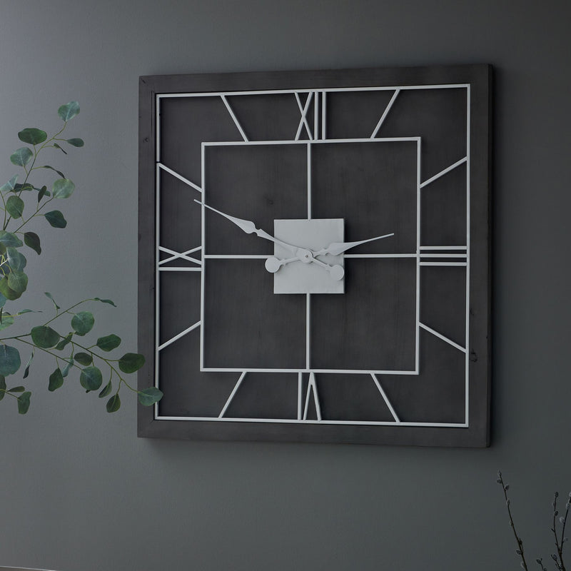 Grey square clock on a dark wall beside trailing greenery